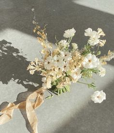 a bouquet of white flowers sitting on top of a cement floor next to a ribbon