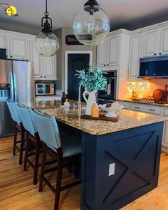 a kitchen with white cabinets and marble counter tops, an island in the middle is surrounded by blue bar stools