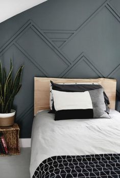 a bed with black and white pillows on top of it next to a potted plant