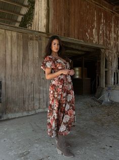 a woman standing in an old barn wearing a floral print dress and gray booties