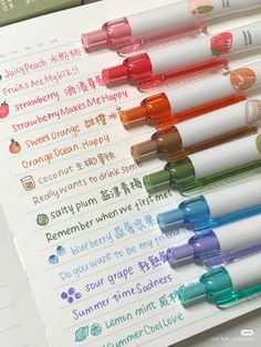 several different colored pens sitting on top of each other next to an open notebook with writing