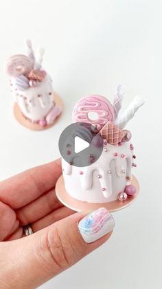 a hand holding a miniature cake with pink and white frosting on it's top