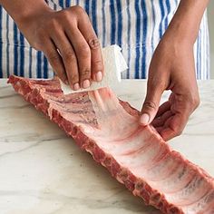 a person cutting up meat on top of a white marble counter with a blue and white striped shirt