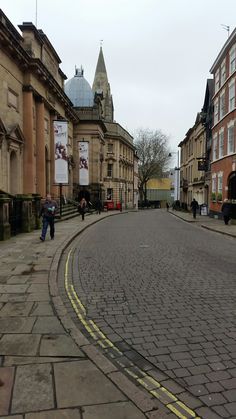 people are walking down the street in an old town with cobblestone roads and tall buildings