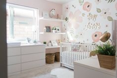 a baby's room decorated in pink and white with flowers on the wall, crib, dressers, and shelves