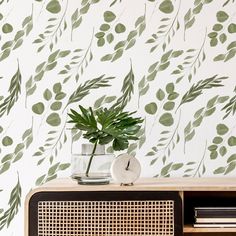 a green plant sitting on top of a wooden cabinet next to a wallpapered wall