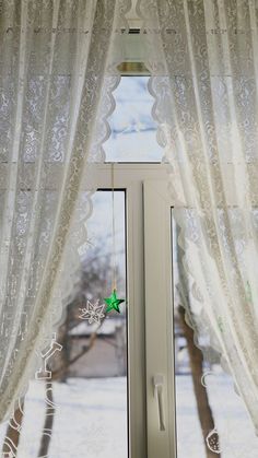 an open window with white curtains and a green star hanging from it's side