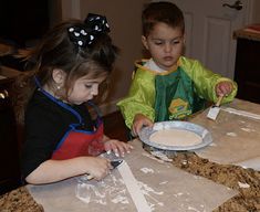 two young children are making paper plates on the kitchen counter