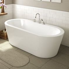 a white bath tub sitting in a bathroom next to a sink and window with pictures on the wall