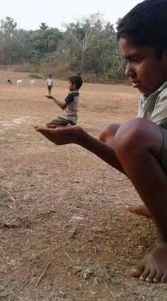 a man sitting on the ground holding out his hand to a small boy who is standing next to him