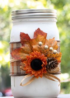 a mason jar decorated with fall leaves and pine cones