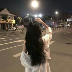 a woman standing in the middle of a street at night with her hands up to her head