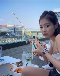 a woman sitting at a table with food and drinks in front of an outdoor stadium