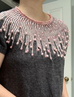 a woman is standing in front of a door wearing a sweater with pink beads on it