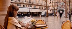 a woman sitting at an outdoor table reading a paper in the middle of a city