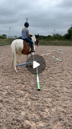 a woman riding on the back of a white and brown horse next to an obstacle