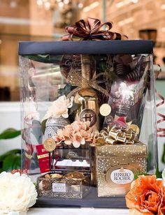 a gift box filled with chocolates and other items sits on a table next to flowers