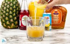 someone pouring orange juice into a glass with pineapples and other drinks in the background