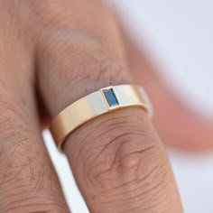 a close up of a person's hand wearing a gold ring with a blue stone