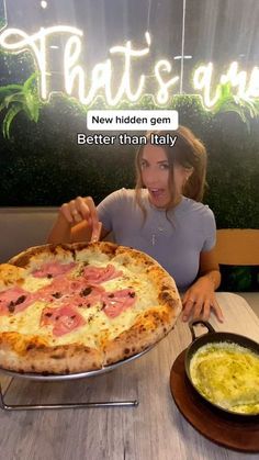 a woman sitting at a table with a pizza in front of her and a bowl of soup to the side