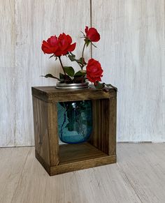 some red flowers are in a blue vase on a wooden stand with white wall behind it