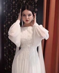 a woman in a white dress is holding her hair up and posing for the camera