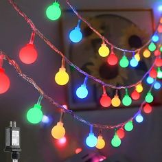 multicolored christmas lights hanging from a string in a room with a phone on the table