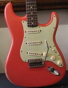 a red and green guitar sitting on top of a blue table next to a window