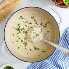 a pot filled with soup next to bread and salad