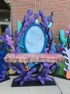 there is a bench made out of purple and blue seaweed on the sidewalk next to a brick building