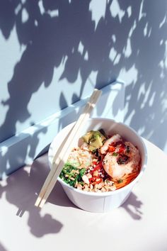 a bowl of food with chopsticks sitting on a table next to a wall