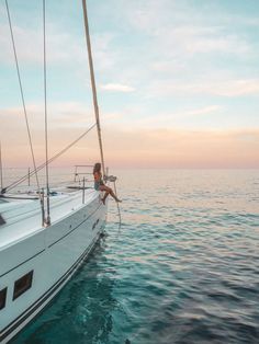 a man sitting on the bow of a sailboat in the ocean at sunset or sunrise