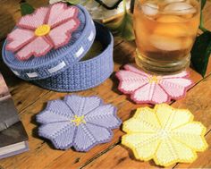 four crocheted flower coasters sitting on a table next to a drink glass