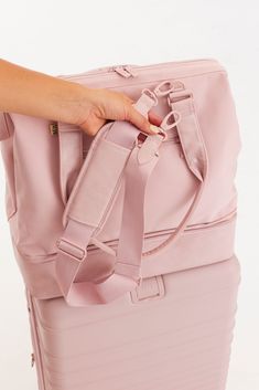 a woman's hand is pulling the handle on a pink piece of luggage with straps