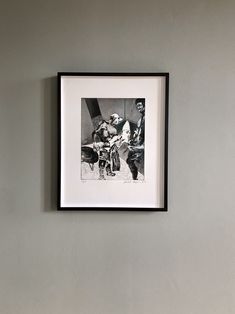 a black and white photo hanging on the wall next to a framed photograph with a man sitting in a chair