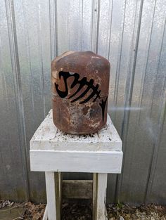 an old rusted metal container sitting on top of a white wooden stool in front of a corrugated wall