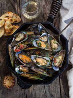 grilled mussels with white wine sauce in a cast iron skillet on a wooden table