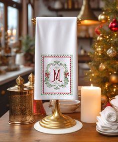 a kitchen towel with a monogrammed christmas wreath on it next to a candle