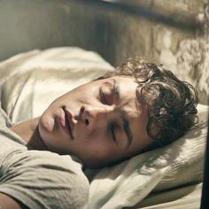 a young man laying in bed with his eyes closed and head resting on the pillow