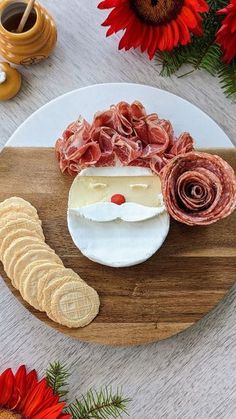 a wooden cutting board topped with cheese, meat and bread slices next to red flowers