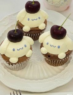 three cupcakes with white frosting and cherries on top are sitting on a plate