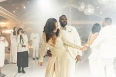 a man and woman dance together on the dance floor in front of other people wearing white tuxedos