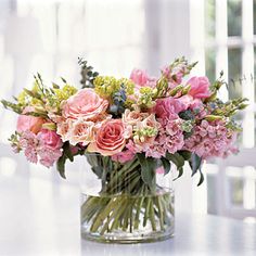 a vase filled with lots of pink flowers on top of a white table next to a window