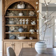 a dining room table with plates and vases on it's china cabinet in front of the wall