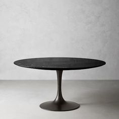 an oval table with black marble top on a white floor in front of a concrete wall