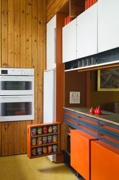 an orange and white kitchen with wood paneling on the walls, stoves and cabinets