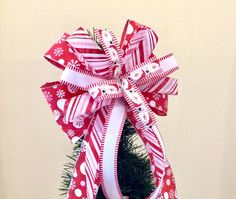 a red and white bow on top of a small christmas tree with snowflakes