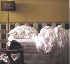 a bed with white sheets and pillows in a bedroom next to a lamp on a table