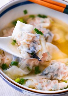 a white bowl filled with dumplings and soup next to chopsticks on a table