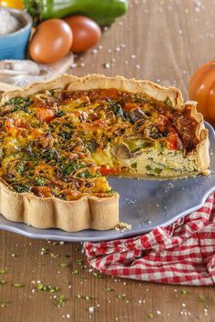 a quiche on a plate with one slice taken out and vegetables in the background